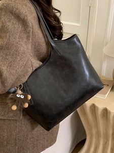Vintage black faux leather tote bag with plush charm on display in a warm room setting