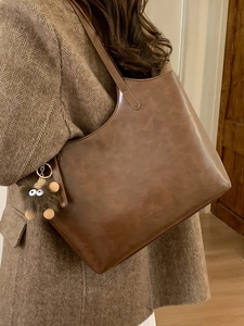 Dark brown leather tote bag with plush monster charm on model wearing brown coat