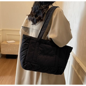 Detailed view of black quilted tote bag with diamond pattern carried by model in a coat