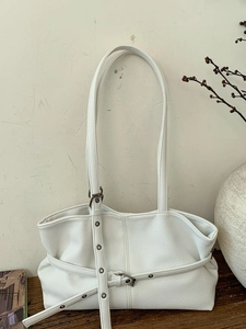 Minimalist white tote bag with lychee texture and silver buckles on a wooden table