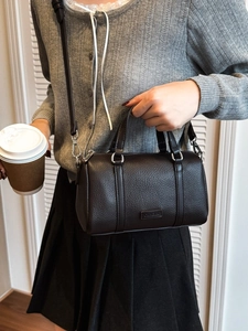 Dark brown leather Boston bag with double handles and shoulder strap held by model