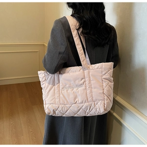 Rear view of a light pink quilted puffer tote bag worn by a model in a gray winter coat