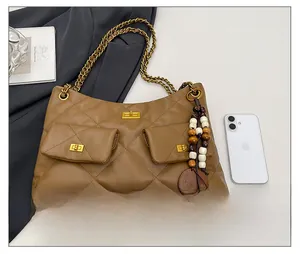 Detail view of brown quilted shoulder bag with chain straps next to a smartphone