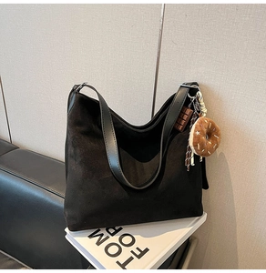 Detail of black suede tote bag with chocolate charm and adjustable leather strap