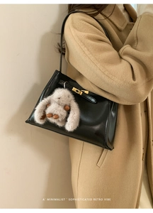 Detail of black glossy bucket bag featuring metal twist lock and plush rabbit charm