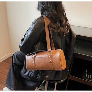 Detail of brown cylinder Boston bag with large metal rings and textured faux leather