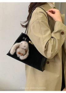 Detail of retro black leather bucket bag with gold lock and plush rabbit pendant charm