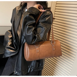 Detail of a brown cylinder Boston bag with dual handles and metallic rivet accents