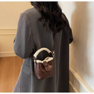 Détail d'un mini sac seau en cuir marron avec bordure en laine de mouton blanche sur costume