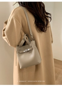 Detail of grey lychee leather bucket bag with silver buckle worn on camel wool coat