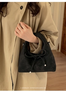Detail of a black suede handbag featuring a bow tie with silver beads and retro vibe