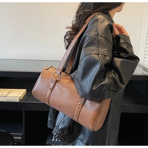 Close-up of brown matte leather cylindrical bag with metallic ring details and stitching