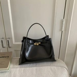 Close-up of a black trapezoid bucket bag with a golden turn-lock on a cream sofa