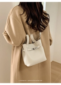 White bucket bag with silver clasp shown on camel wool coat for a retro vibe