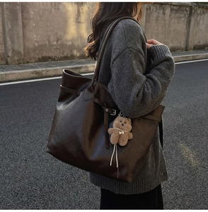 Detailed close-up of dark brown tote bag featuring matte leather texture and cute bear charm