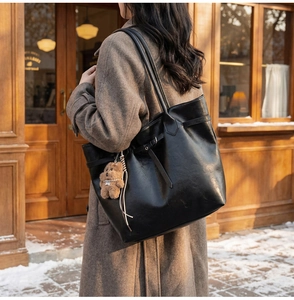 Detail of black faux leather tote bag with brown plush bear charm in a winter street setting
