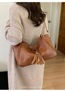 Detail of vintage brown leather hobo bag featuring tassel decor and woven stitching