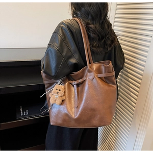 Close-up of vintage brown leather tote bag side with metal buckle and teddy bear charm