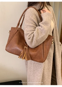Detail of brown faux leather tote bag with fringe charm and woven stitching details
