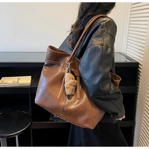 Detail of dark brown tote bag featuring matte leather texture and plush bear accessory