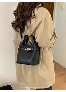 Detail of black pebbled leather bucket bag with silver turn-lock clasp worn by model