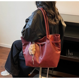 Detail of burgundy leather tote bag with decorative buckle and plush bear charm accessory