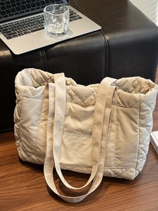 Quilted cream tote bag with letter embroidery on dark wood and office background