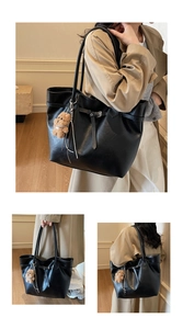 Detail of a large black faux leather tote bag with a plush bear charm and long straps