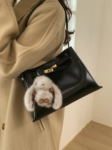 Retro black bucket bag with gold lock and plush rabbit charm on camel wool coat