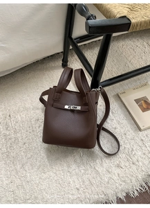 Detail of dark brown leather bucket bag with silver clasp on white plush carpet