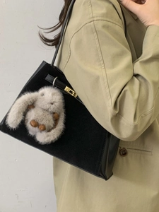Minimalist black suede bucket bag with gray fur pendant worn with a khaki trench coat