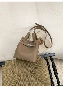 Close-up of minimalist pebble leather bucket bag with silver twist lock on a vintage chair