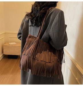 Detailed side view of brown suede tote bag with long fringes worn on model shoulder
