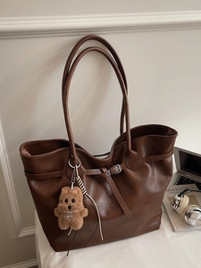 Brown faux leather tote bag with bear charm and adjustable strap on a minimalist desk