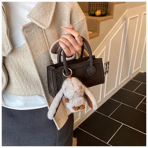 Detailed shot of dark brown mini handbag featuring a soft grey plush bunny charm