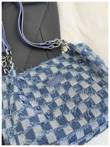 Detail of blue checkerboard denim tote bag with frayed edges and fashion leather label