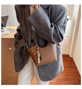 Nahaufnahme der braunen Leder-Eimertasche mit Webstruktur und Vintage-Perlenanhänger
