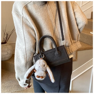 Detail of dark brown handbag with cylinder handles and a cute white bunny plush charm
