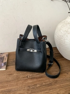 Classic black leather bucket bag with silver buckle on a wooden desk with home decor