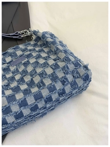 Close-up of blue and white checkerboard denim tote bag with frayed edges and metal zipper
