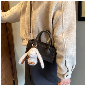 Detail of dark gray matte leather crossbody bag featuring a soft plush bunny charm