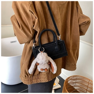 Black leather small square bag with plush bunny pendant on brown corduroy coat