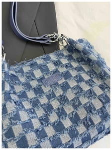Detailed macro view of checkered denim tote bag with frayed edges and leather brand tag