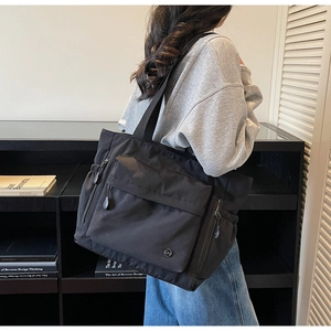 Detail of a large black nylon tote bag with functional zipper pockets and durable straps