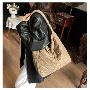 Detail of a large quilted puffy tote bag in beige with square stitching on a wide strap