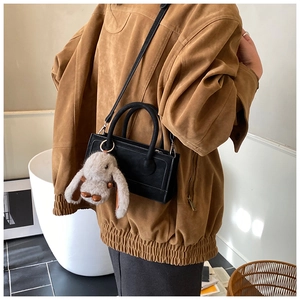 Detail of black leather crossbody bag with cute plush bunny charm on a model