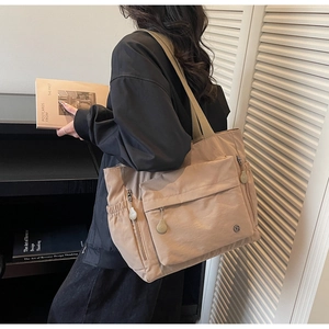 Detail of large khaki nylon tote bag featuring front utility pockets and wide strap