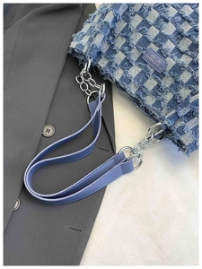 Detail of blue checkerboard denim tote with distressed edges and silver chain strap