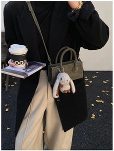 Deep green mini crossbody bag with plush bunny charm and dual top handles in autumn setting