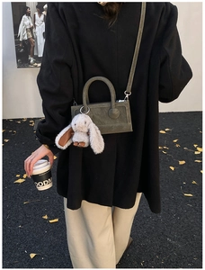 Detail of grey crossbody bag with fuzzy rabbit charm held by model in autumn street scene